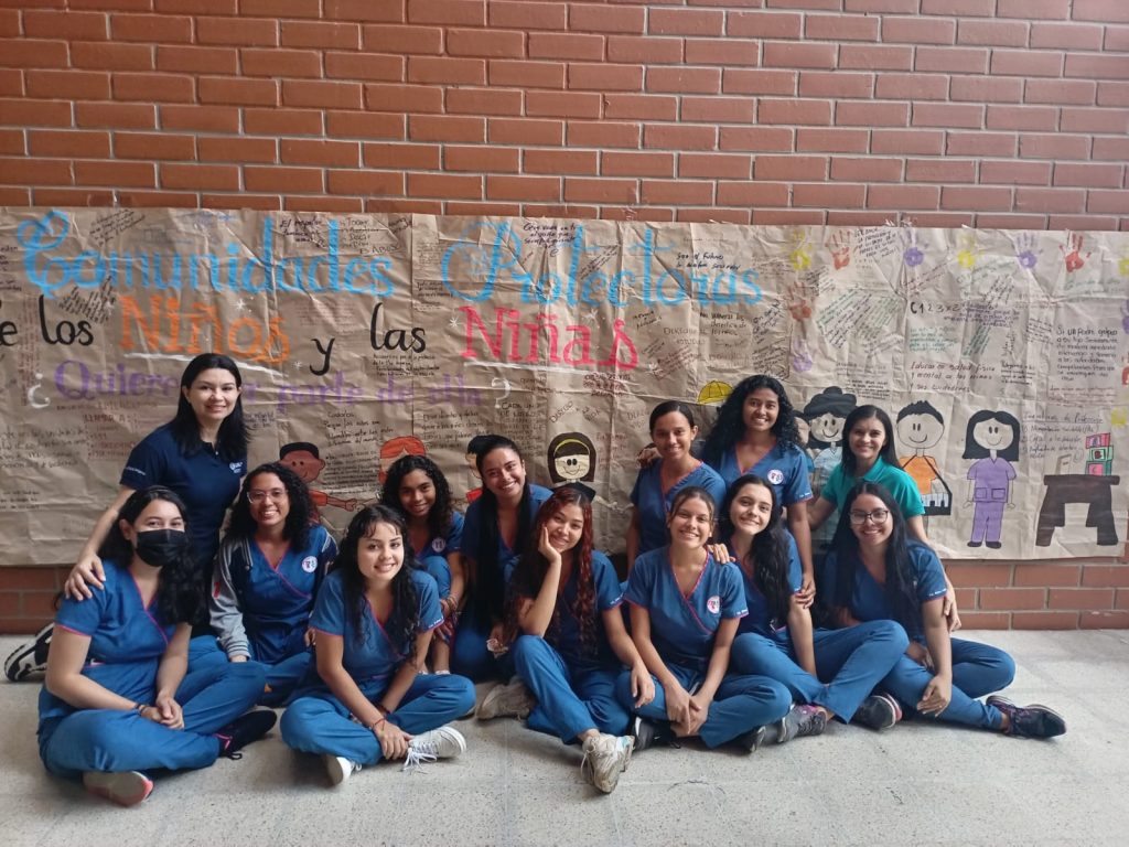 Estudiantes de quinto semestre del programa de Licenciatura en Educación Infantil frente al mural donde participaron las personas de la comunidad académica sobre el tema de comunidades protectoras.